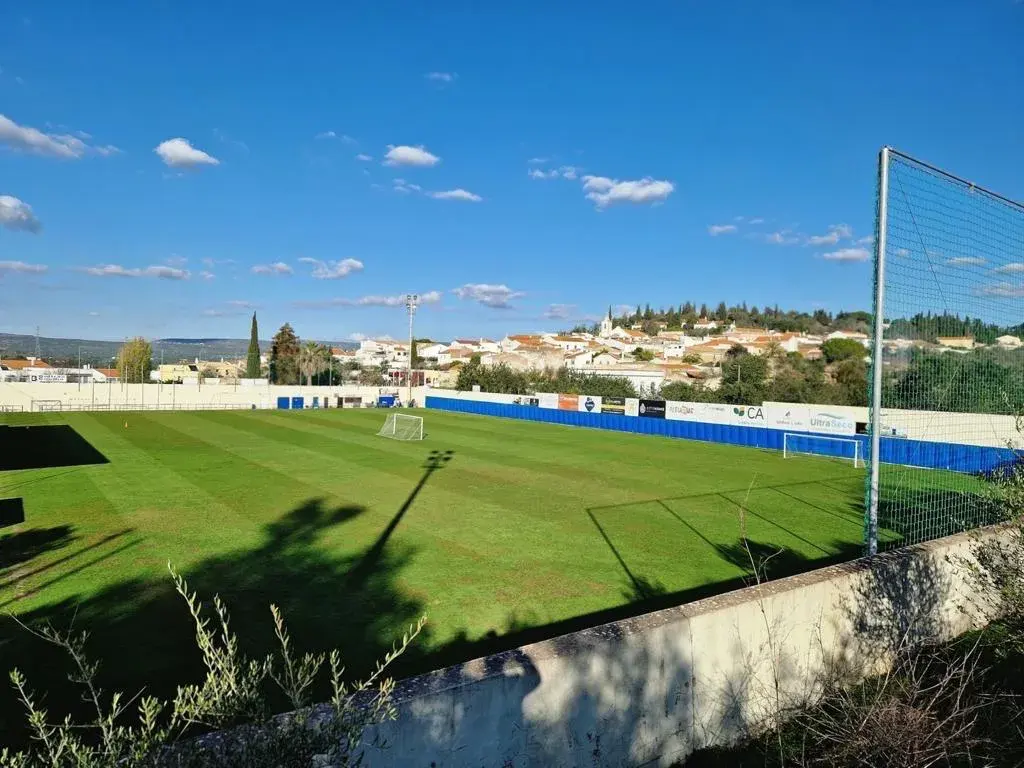 O relvado do Estádio João Campos, com as casas de Paderne por trás